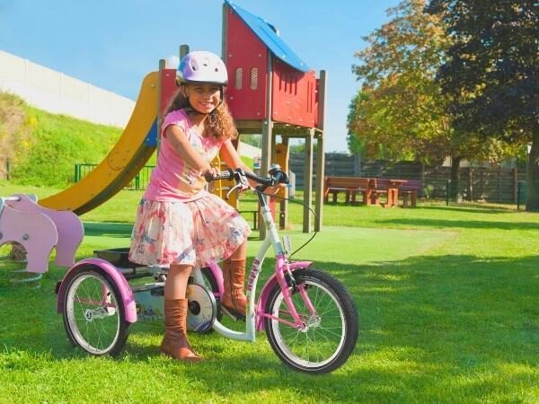 Fietsen - meisje op speelplein op haar roze driewielfiets